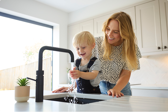 L’enfant se lave les mains dans la cuisine pendant que sa mère le regarde L’enfant se lave les mains dans la cuisine pendant que sa mère le regarde